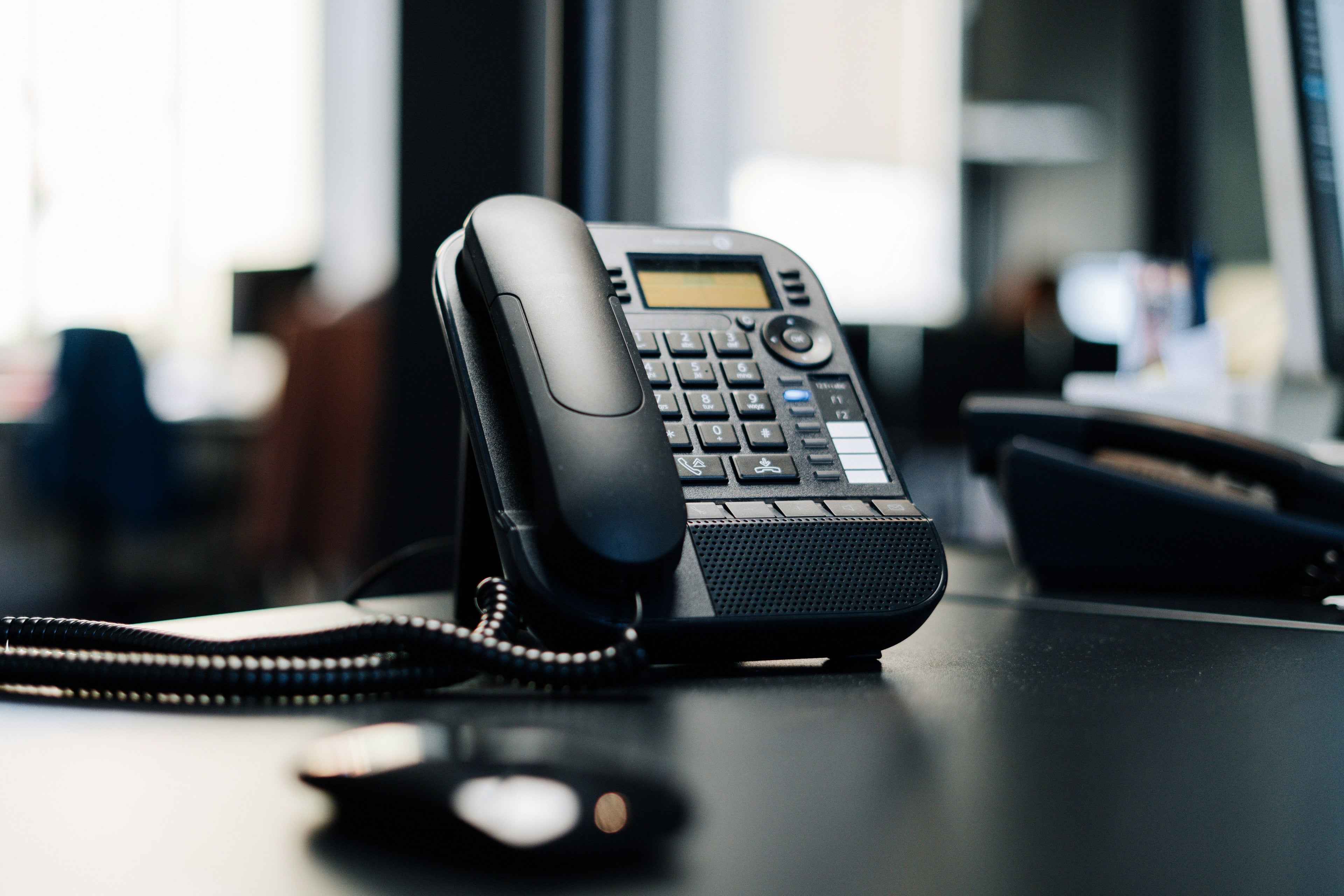 Black office phone on a desk with a blurred office background